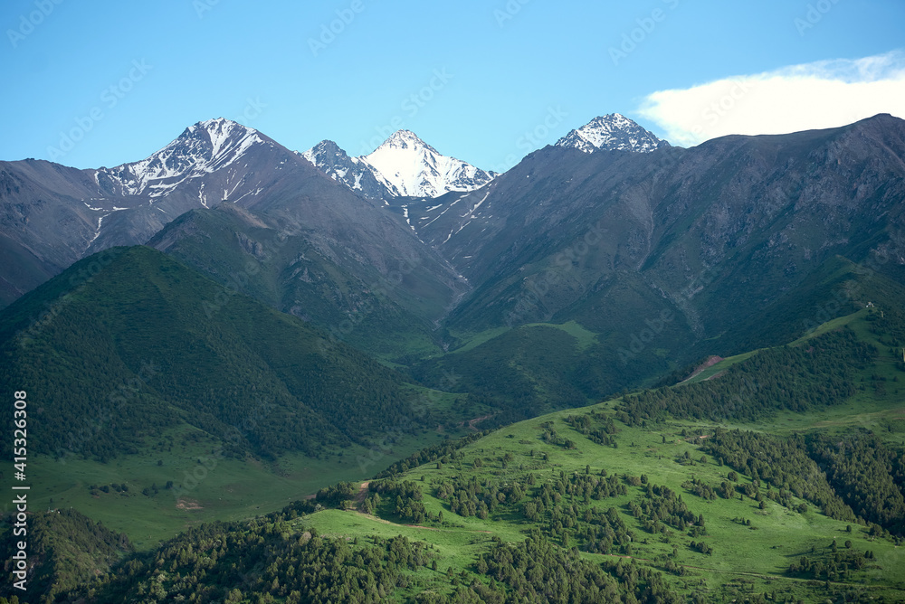 The nature of Kyrgyzstan. Summer. Mountain landscape. Among green valleys, mountains are visible at middle of the day. Tien Shan Mountains, Kyrgyzstan.