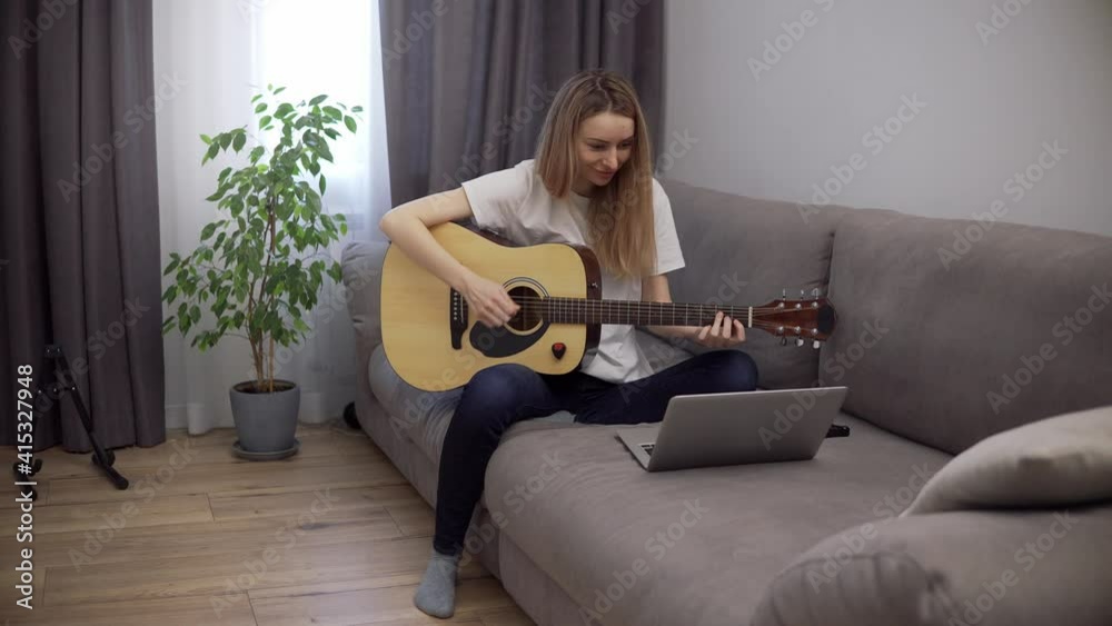 Portrait of a woman plays the guitar through a video call on a laptop, leaning chords Portrait of a woman plays the guitar through a video call on a laptop, leaning chords