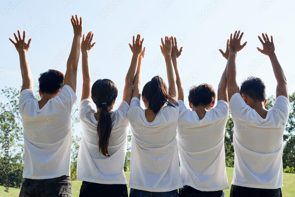 © DragonImages - Happy excited young people in white t-shirts raising arms when standing in city park, view from the back