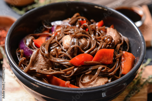 Plate with tasty soba noodles and meat on dark background