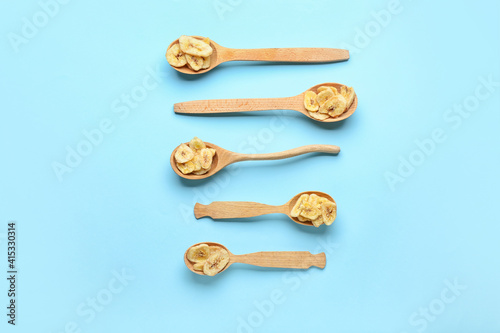 Spoons with crispy banana chips on color background