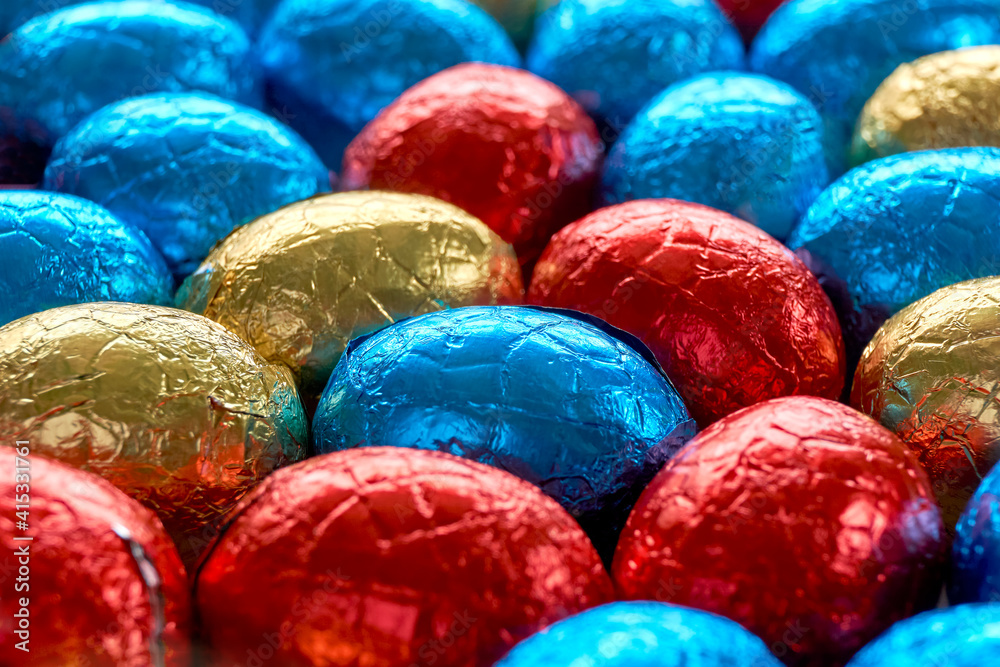 Closeup of many chocolate easter eggs wrapped in blue, red and golden foil. Easter background with selective focus. Closeup of many chocolate easter eggs wrapped in blue, red and golden foil. Easter background with selective focus.