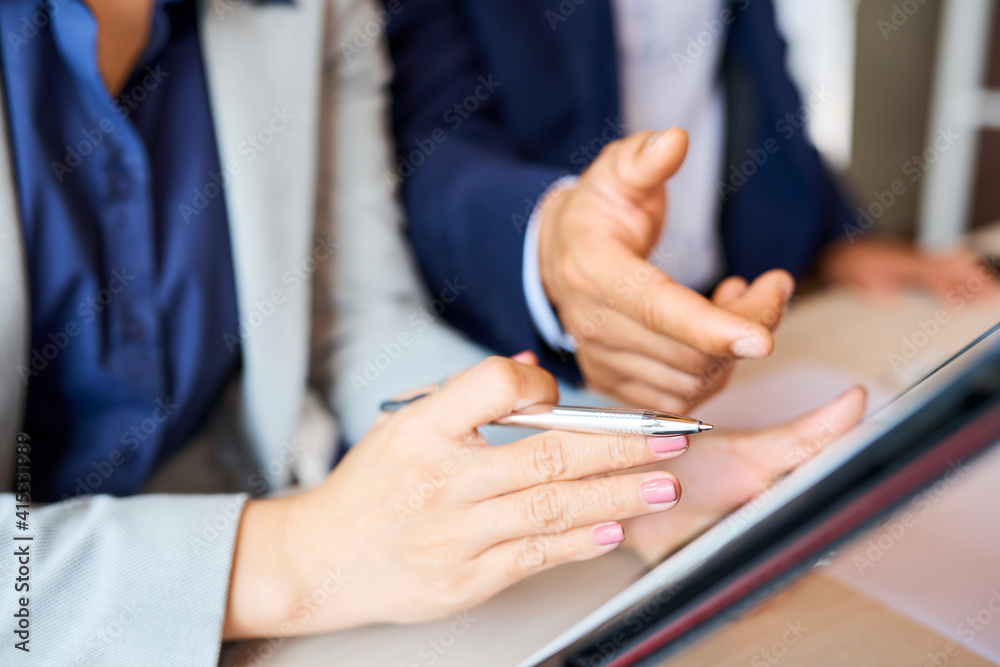 Close-up image of business people pointing at tablet computer and discussing article or report