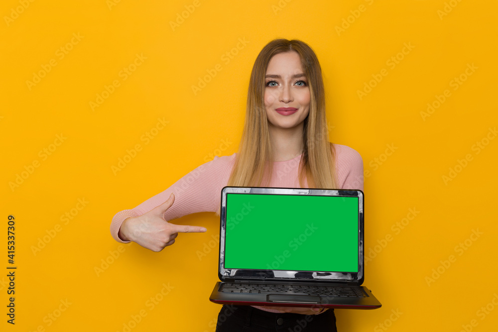 Naklejka premium Smiling Girl Is Holding Laptop With Green Screen And Pointing At It.