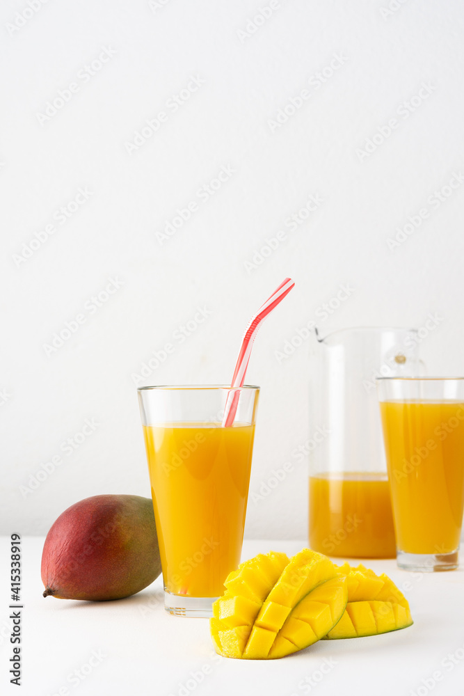 Mango juice in a glass jug and glasses with juice and a straw on a white background, chopped mango and whole, delicious healthy sweet natural drink Mango juice in a glass jug and glasses with juice and a straw on a white background, chopped mango and whole, delicious healthy sweet natural drink