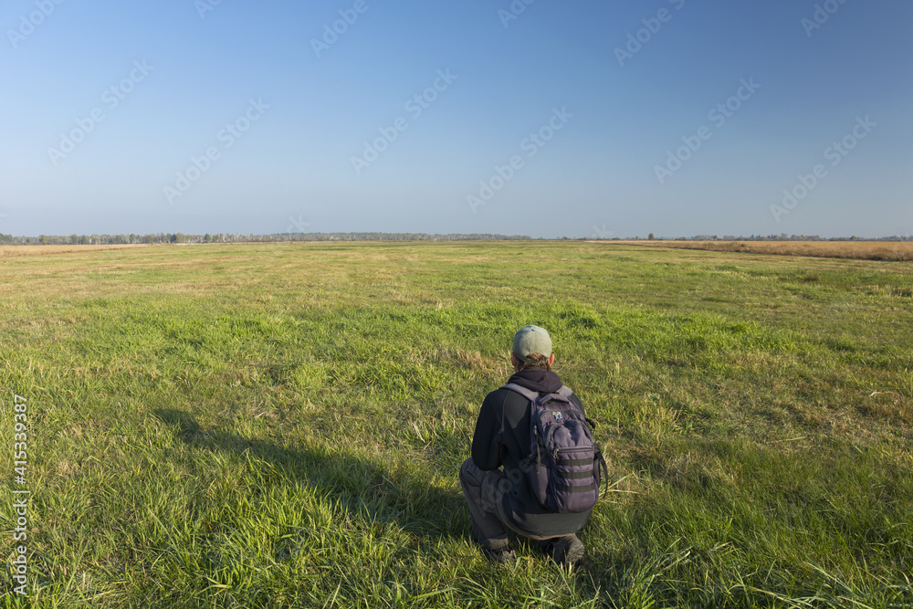 A traveler with a backpack will crouch on the meadow, Srebrzyszcze, Poland