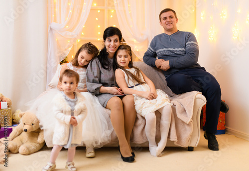 family portrait - parents and children in home interior decorated with holiday lights and gifts