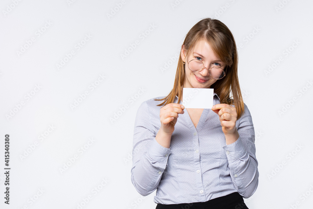 A beautiful smiling woman in a blue shirt with glasses holds and shows a blank card or company business card. Promotion concept. A beautiful smiling woman in a blue shirt with glasses holds and shows a blank card or company business card. Promotion concept.