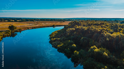 Aerial view of a beautiful summer landscape over river while dawn. Top view over river with a smooth water surface reflecting blue sky.