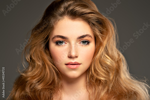 Closeup portrait of an young adult girl with long curly hair. Photo of a fashion model posing at studio. Pretty young woman with long brown hair looking at camera. Beauty portrait.