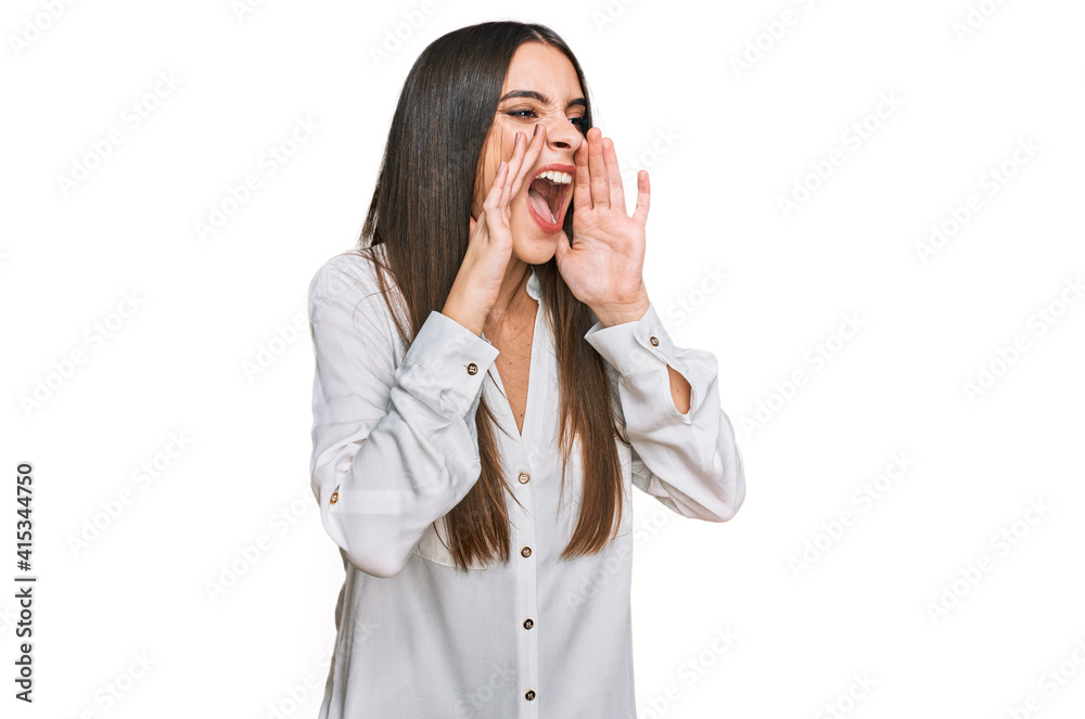 Young beautiful woman wearing casual white shirt shouting angry out loud with hands over mouth Young beautiful woman wearing casual white shirt shouting angry out loud with hands over mouth