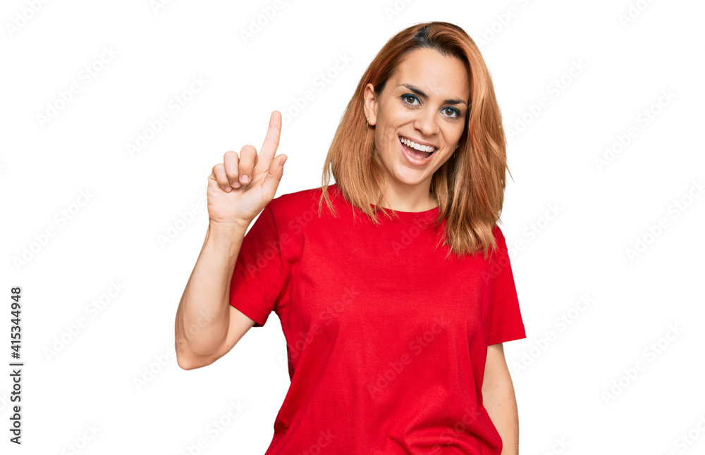 Hispanic young woman wearing casual red t shirt showing and pointing up with finger number one while smiling confident and happy.