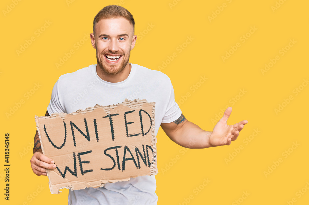 Young irish man holding united we stand banner celebrating victory with happy smile and winner expression with raised hands Young irish man holding united we stand banner celebrating victory with happy smile and winner expression with raised hands