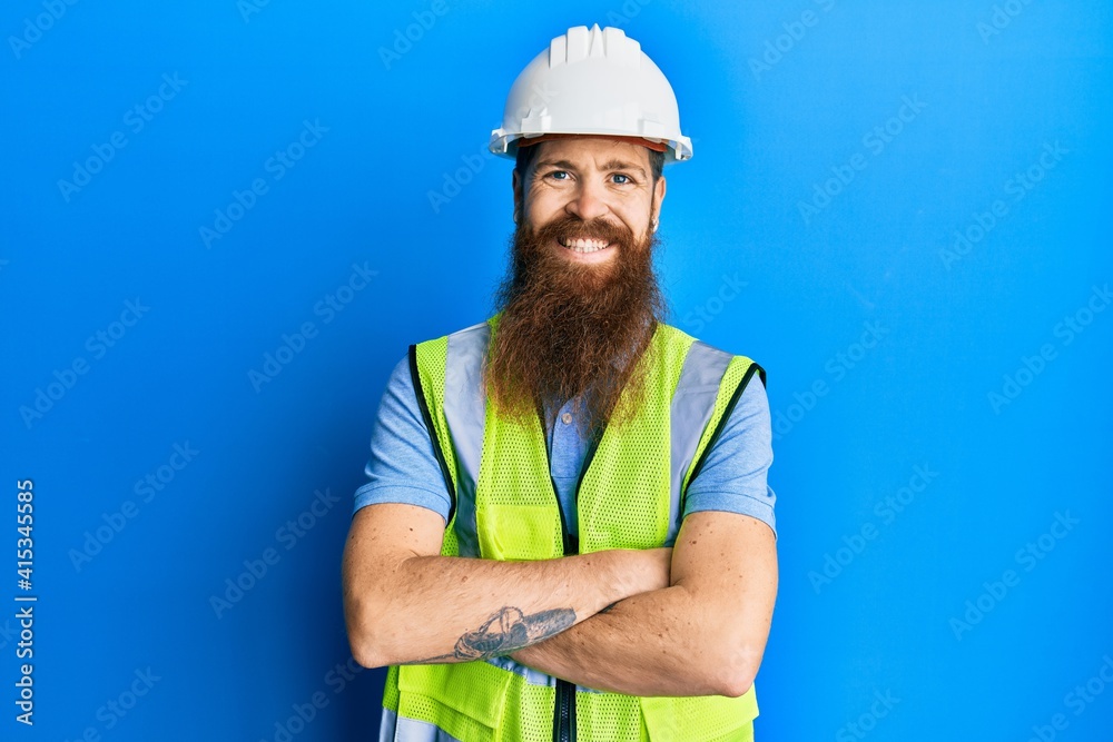 Redhead man with long beard wearing safety helmet and reflective jacket happy face smiling with crossed arms looking at the camera. positive person. Redhead man with long beard wearing safety helmet and reflective jacket happy face smiling with crossed arms looking at the camera. positive person.