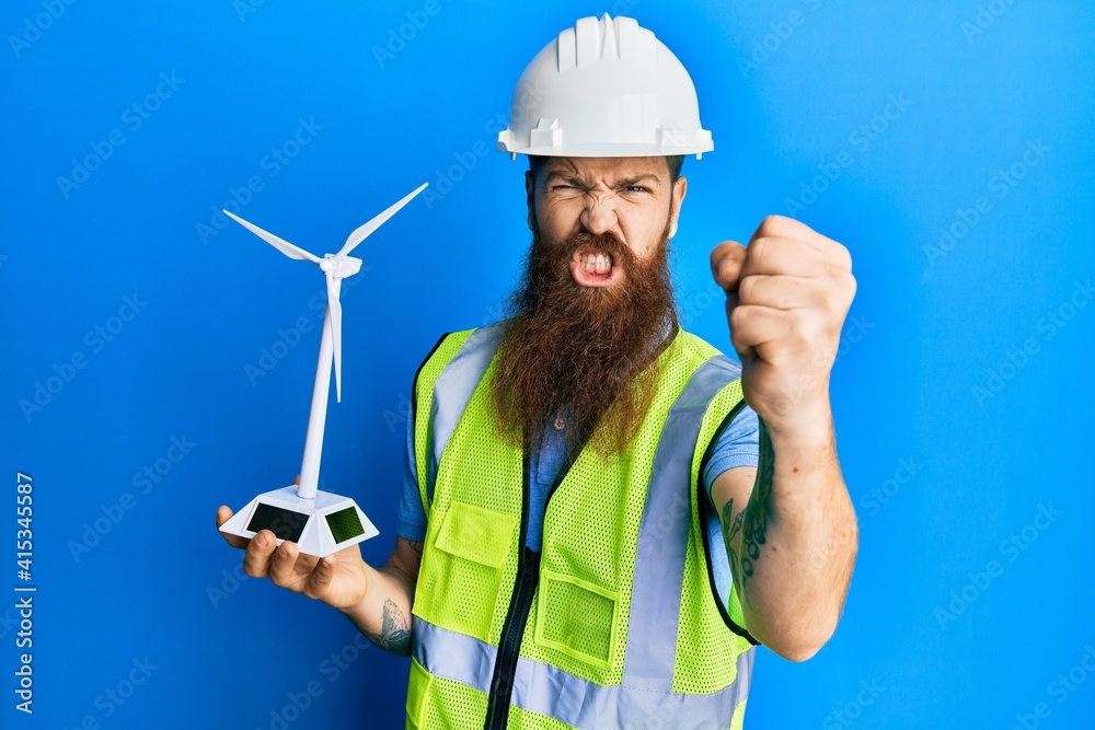 Redhead man with long beard holding solar windmill for renewable electricity annoyed and frustrated shouting with anger, yelling crazy with anger and hand raised