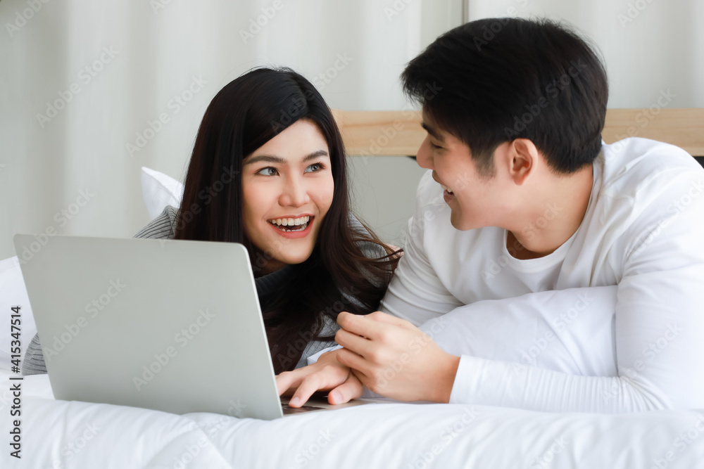 Young Asian black long hair woman and clear face man lovers laying on bed and using notebook computer to serf internet together with relax and happy Young Asian black long hair woman and clear face man lovers laying on bed and using notebook computer to serf internet together with relax and happy