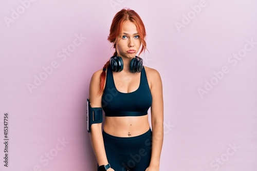 Valokuvatapetti Young beautiful redhead woman wearing gym clothes and using headphones depressed and worry for distress, crying angry and afraid