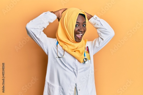 Beautiful african young woman wearing doctor uniform and hijab relaxing and stretching, arms and hands behind head and neck smiling happy © Krakenimages.com