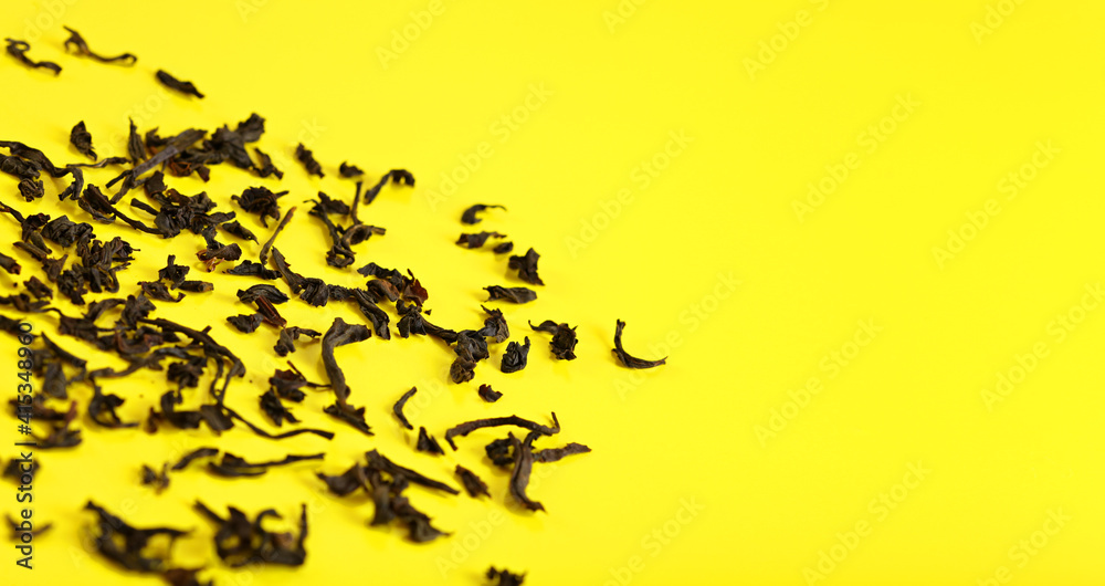 Dry black loose tea leaves on yellow board, closeup detail from above, space for text right side