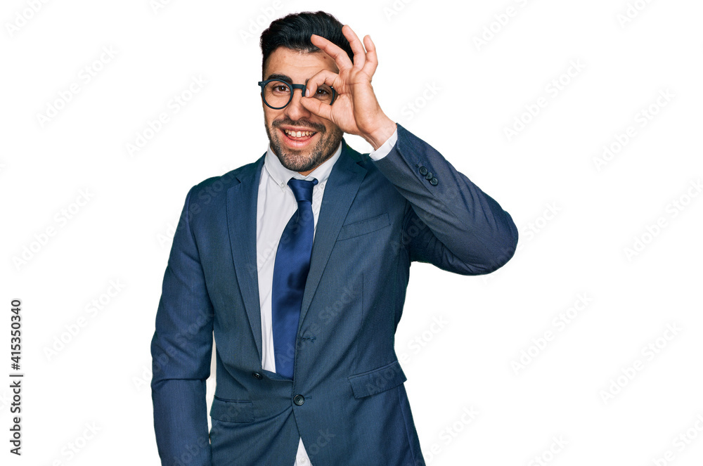 Hispanic man with beard wearing business suit and tie smiling happy doing ok sign with hand on eye looking through fingers Hispanic man with beard wearing business suit and tie smiling happy doing ok sign with hand on eye looking through fingers