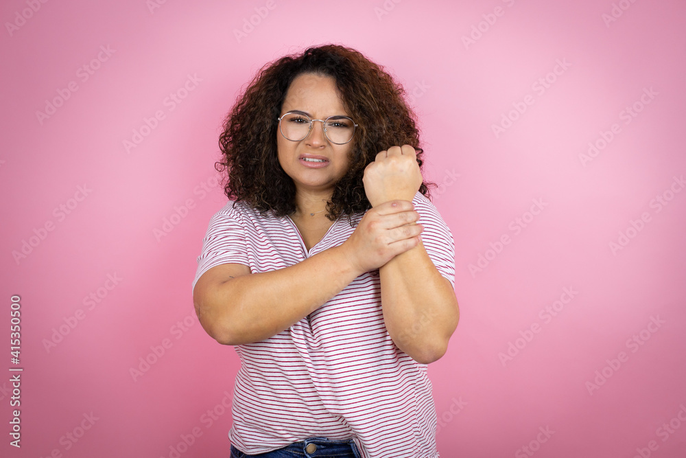 Young african american woman wearing red stripes t-shirt over pink background suffering pain on hands and fingers, arthritis inflammation Young african american woman wearing red stripes t-shirt over pink background suffering pain on hands and fingers, arthritis inflammation