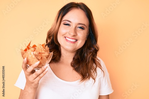 Young beautiful caucasian woman holding nachos potato chips looking positive and happy standing and smiling with a confident smile showing teeth