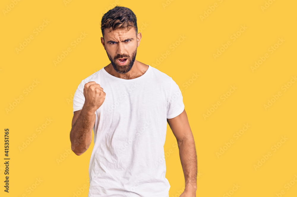 Young hispanic man wearing casual white tshirt angry and mad raising fist frustrated and furious while shouting with anger. rage and aggressive concept. Young hispanic man wearing casual white tshirt angry and mad raising fist frustrated and furious while shouting with anger. rage and aggressive concept.
