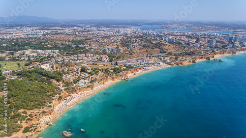 Aerial drone shot of a busy beach, amazing cliffs, vegetation and also buidlings in the background. Praia do Vau, Portimao, Portugal. © sergojpg