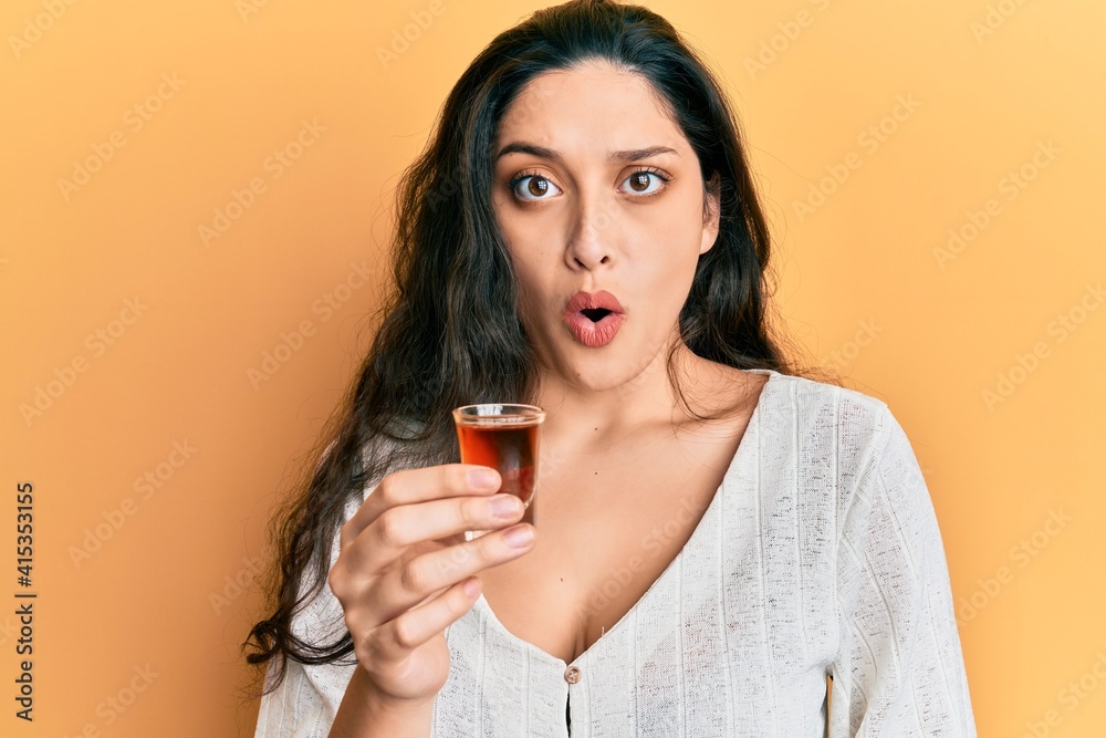Beautiful middle eastern woman drinking whiskey shot scared and amazed with open mouth for surprise, disbelief face