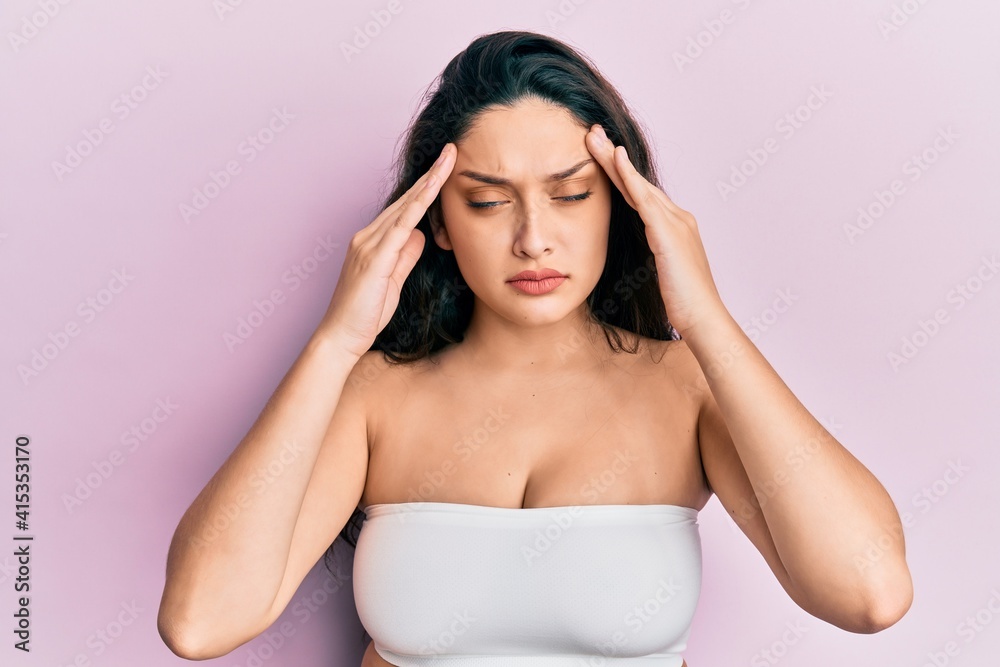 Beautiful middle eastern woman standing wearing a top showing skin with hand on head, headache because stress. suffering migraine. Beautiful middle eastern woman standing wearing a top showing skin with hand on head, headache because stress. suffering migraine.