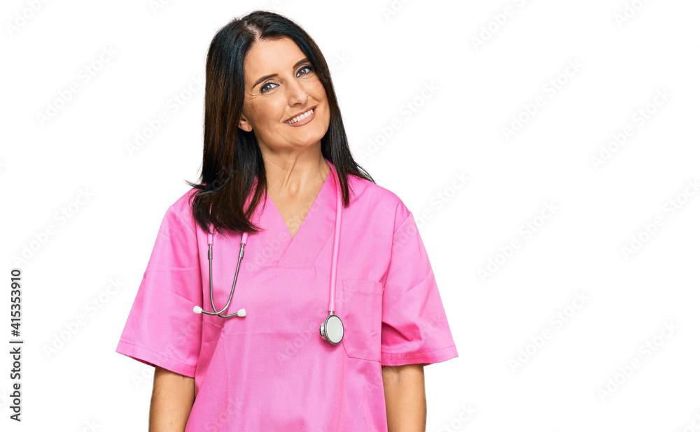 Middle age brunette woman wearing doctor uniform and stethoscope looking positive and happy standing and smiling with a confident smile showing teeth Middle age brunette woman wearing doctor uniform and stethoscope looking positive and happy standing and smiling with a confident smile showing teeth