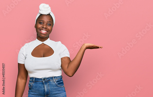 Young african woman with turban wearing hair turban over isolated background smiling cheerful presenting and pointing with palm of hand looking at the camera.