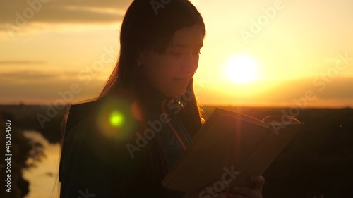 A girl holds Bible in his hands and studies word of God at sunrise on top of mountain. A woman reads a book in rays of the sun. Man reads Bible outdoors. Searching for truth in scriptures.