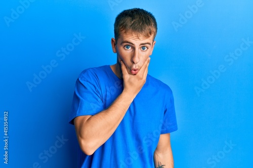 Young caucasian man wearing casual blue t shirt looking fascinated with disbelief, surprise and amazed expression with hands on chin