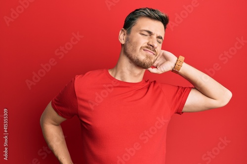 Handsome caucasian man wearing casual red tshirt suffering of neck ache injury, touching neck with hand, muscular pain