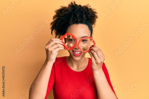 Young african american girl holding red pepper as a glasses smiling and laughing hard out loud because funny crazy joke.