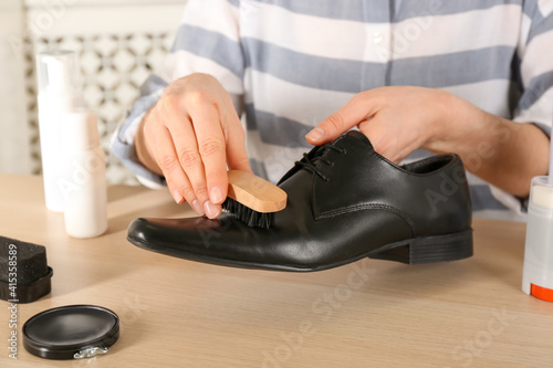 Woman cleaning stylish footwear at wooden table  closeup. Shoe care accessories