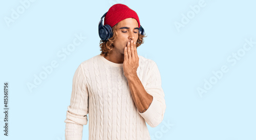 Young hispanic man listening to music using headphones bored yawning tired covering mouth with hand. restless and sleepiness. © Krakenimages.com