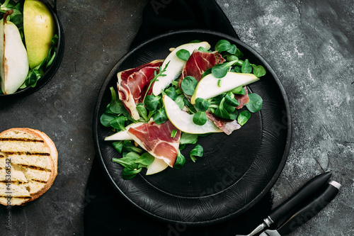 Parma, pear and spinach salad on black plate