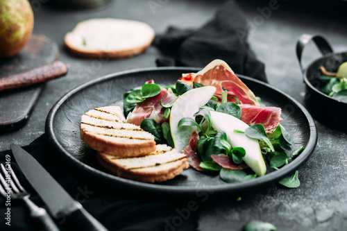 Parma, pear and spinach salad on black plate