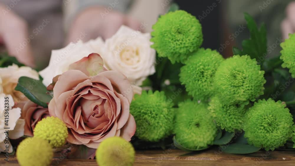 Panning close up of freshly picked flowers lying on wooden table in flower shop, while professional florists arranging them in beautiful bouquet