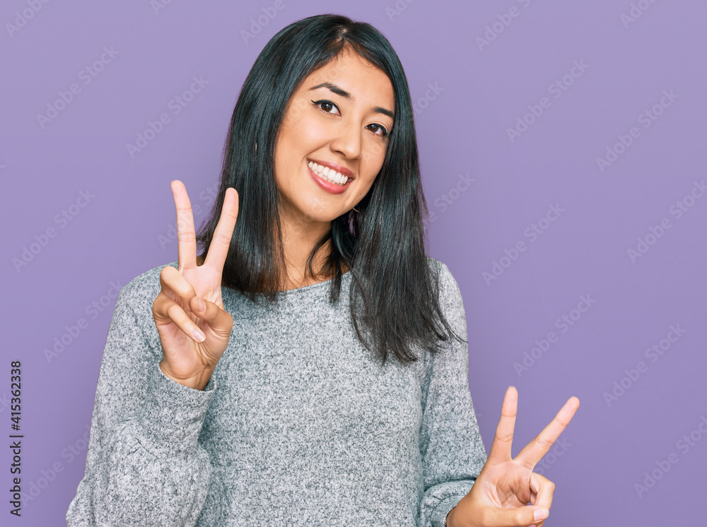 Beautiful asian young woman wearing casual clothes smiling looking to the camera showing fingers doing victory sign. number two.