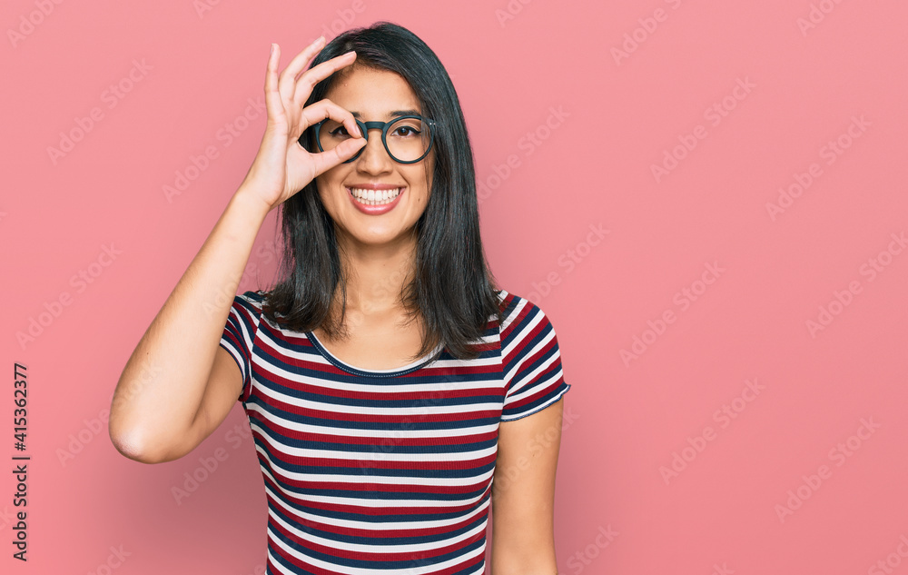 Beautiful asian young woman wearing casual clothes and glasses doing ok gesture with hand smiling, eye looking through fingers with happy face. Beautiful asian young woman wearing casual clothes and glasses doing ok gesture with hand smiling, eye looking through fingers with happy face.