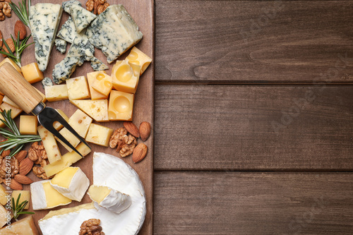 Cheese plate with rosemary and nuts on wooden table, top view. Space for text