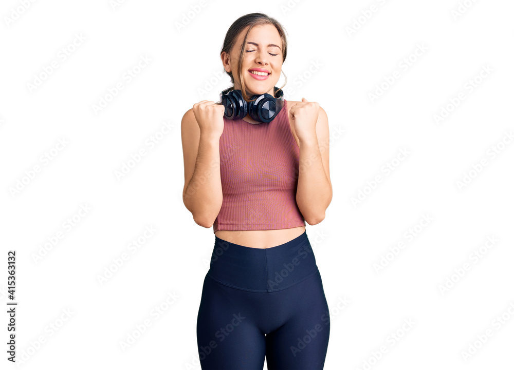Beautiful caucasian young woman wearing gym clothes and using headphones excited for success with arms raised and eyes closed celebrating victory smiling. winner concept.
