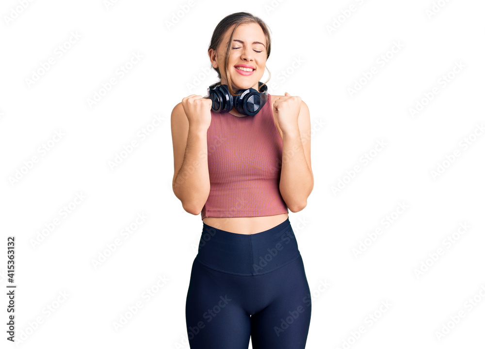 Beautiful caucasian young woman wearing gym clothes and using headphones excited for success with arms raised and eyes closed celebrating victory smiling. winner concept. Beautiful caucasian young woman wearing gym clothes and using headphones excited for success with arms raised and eyes closed celebrating victory smiling. winner concept.