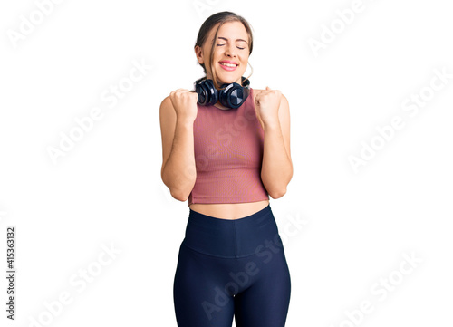 Beautiful caucasian young woman wearing gym clothes and using headphones excited for success with arms raised and eyes closed celebrating victory smiling. winner concept.