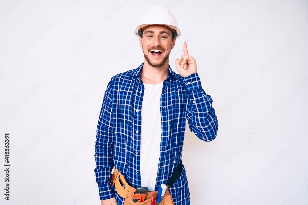 Young handsome man weaing handyman uniform pointing finger up with successful idea. exited and happy. number one. Young handsome man weaing handyman uniform pointing finger up with successful idea. exited and happy. number one.