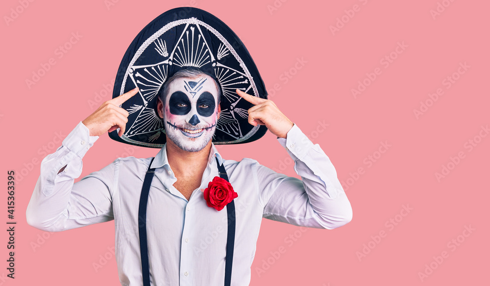 Man wearing day of the dead costume over background smiling pointing to head with both hands finger, great idea or thought, good memory Man wearing day of the dead costume over background smiling pointing to head with both hands finger, great idea or thought, good memory