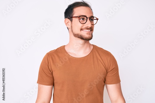 Young handsome man wearing casual clothes and glasses looking away to side with smile on face, natural expression. laughing confident.